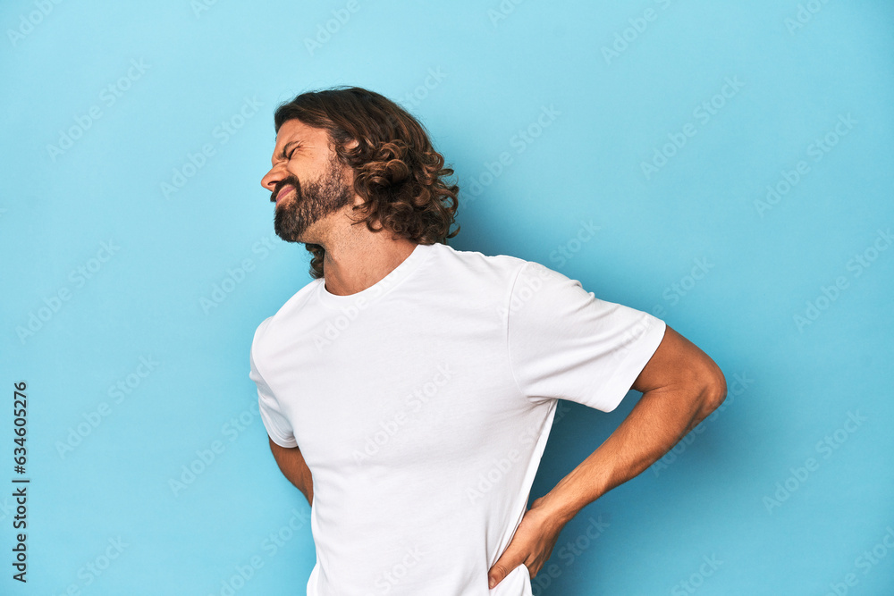 Bearded man in a white shirt, blue backdrop suffering a back pain. Bearded man in a white shirt, blue backdrop suffering a back pain.