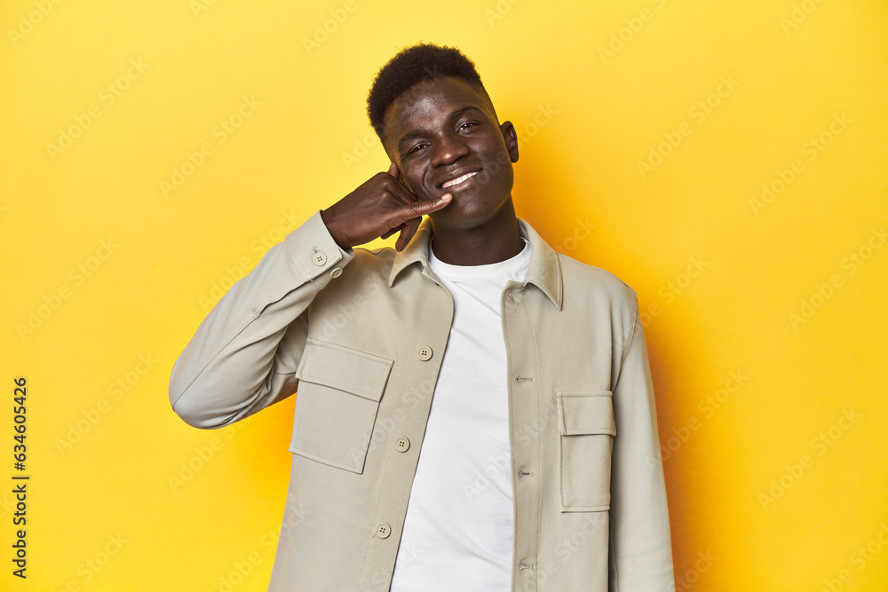 Stylish young African man on vibrant yellow studio background, showing a mobile phone call gesture with fingers. Stylish young African man on vibrant yellow studio background, showing a mobile phone call gesture with fingers.