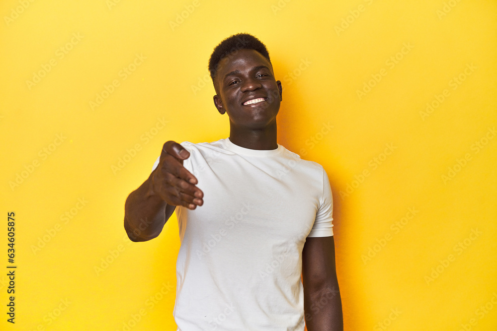 Stylish young African man on vibrant yellow studio background, stretching hand at camera in greeting gesture. Stylish young African man on vibrant yellow studio background, stretching hand at camera in greeting gesture.