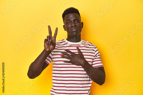Stylish young African man on vibrant yellow studio background, taking an oath, putting hand on chest.