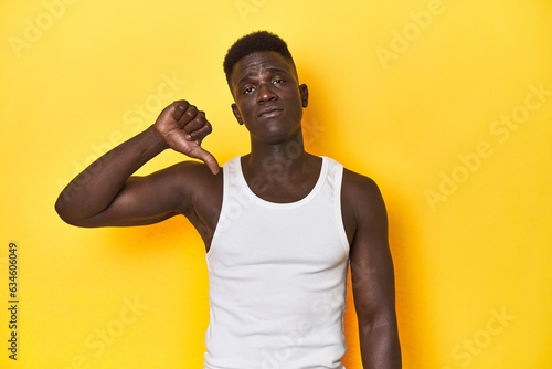 Stylish young African man on vibrant yellow studio background, showing a dislike gesture, thumbs down. Disagreement concept.