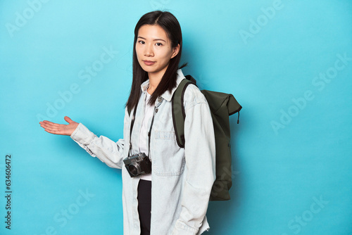 Young Asian traveler ready to capture adventures  showing a copy space on a palm and holding another hand on waist.
