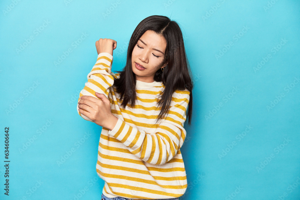 Asian woman in striped yellow sweater, massaging elbow, suffering after a bad movement. Asian woman in striped yellow sweater, massaging elbow, suffering after a bad movement.