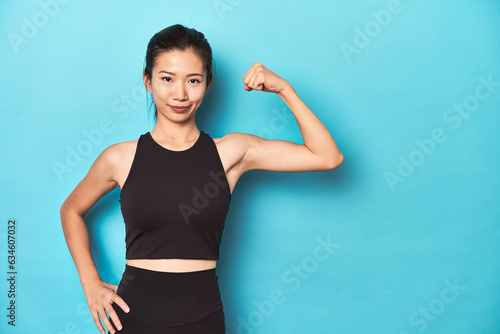 Canvas Print Asian sportswoman showing strength with arm gesture, studio shot.