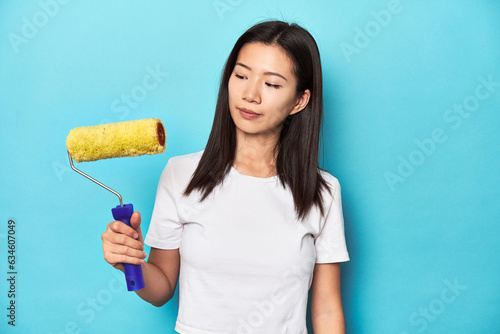 Tableau sur toile Young Asian woman with yellow paint roller, studio shot.