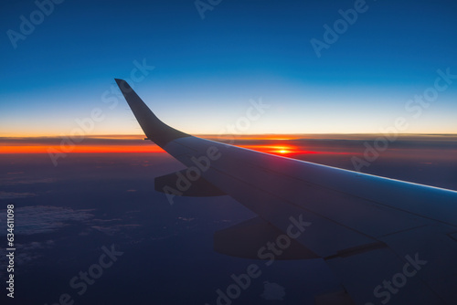Airplane flight in sunset sky over ocean water and wing of plane. View from the window of the Aircraft. Traveling in air.