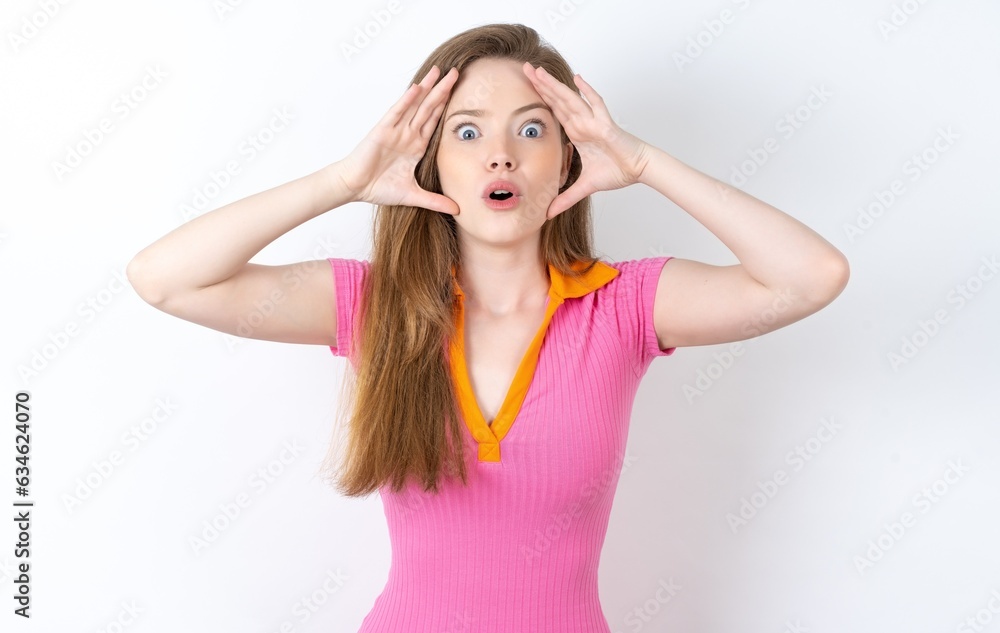 Young woman wearing pink dress with scared expression, keeps hands on head, jaw dropped, has terrific expression. Omg concept Young woman wearing pink dress with scared expression, keeps hands on head, jaw dropped, has terrific expression. Omg concept