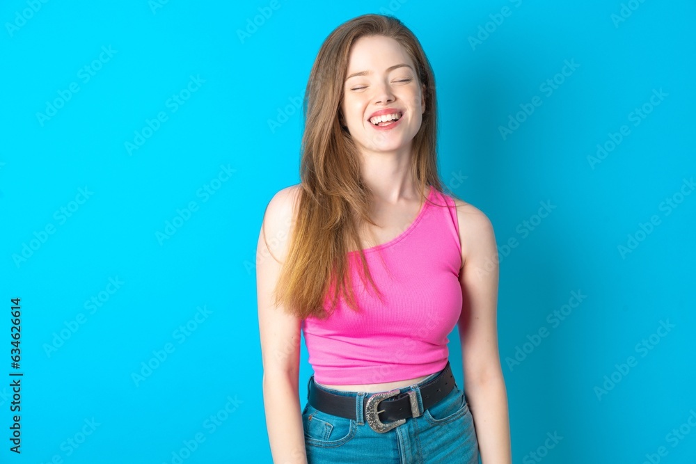 Positive Young beautiful girl wearing pink T-shirt with overjoyed expression closes eyes and laughs shows white perfect teeth Positive Young beautiful girl wearing pink T-shirt with overjoyed expression closes eyes and laughs shows white perfect teeth