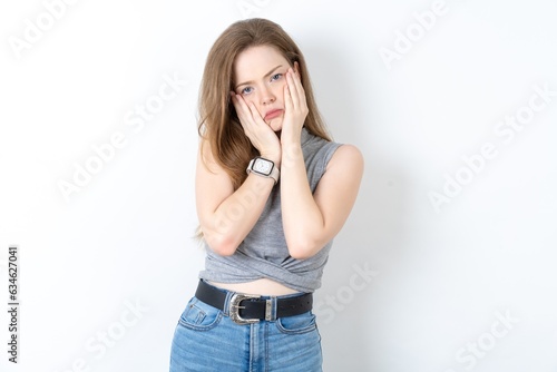 Young beautiful girl wearing grey T-shirt keeps hands on cheeks has bored displeased expression. Stressed hopeless model © Roquillo