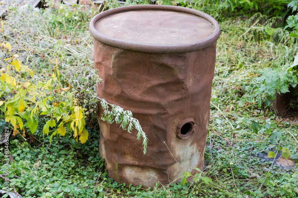 Old rusty iron barrel with dents outdoors among the grass