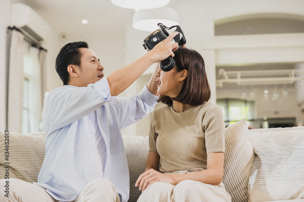 Husband wearing VR to wife and playing game on sofa at home