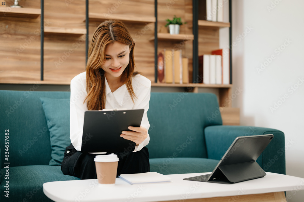 Young beautiful woman using laptop and tablet while sitting at her working place. Concentrated at work. in living room on the sofa at home office.
