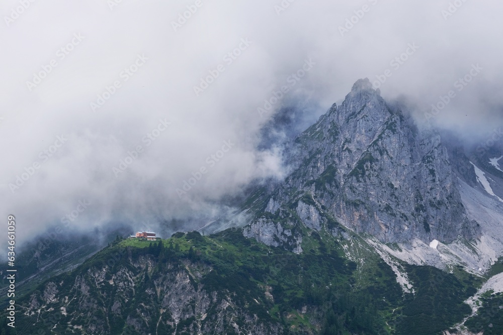 Dramatic scenery of mountain peaks among clouds and Hofpurglhutte shelter building, Dachstein Massif, Austrian Alps