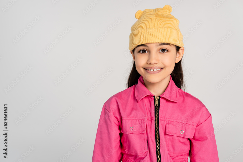 happy girl in yellow beanie hat and pink outfit looking at camera on grey backdrop, stylish kid happy girl in yellow beanie hat and pink outfit looking at camera on grey backdrop, stylish kid