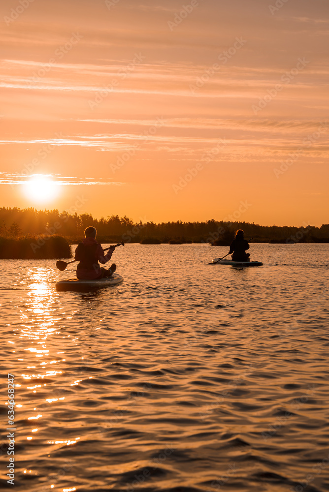 Stand up paddle boarding or standup paddleboarding on quiet lake at sunrise with beautiful colors during warm summer. Active women, close-up of water surface.