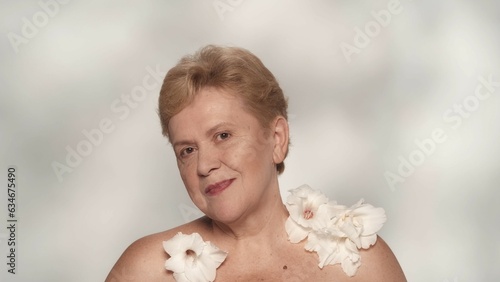 Beautiful blonde aged woman posing, smiling at the camera with a white gladiolus flowers