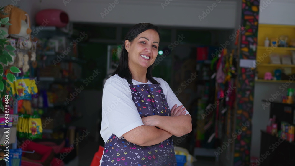 Cheerful Female Pet Shop Owner in Apron Poses for Camera with arms crossed. Confident Small Business Owner from South America