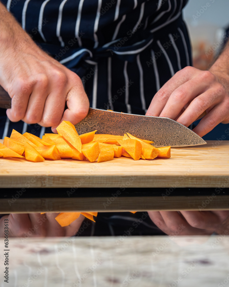 chef hands cutting fresh carrots in slices with a kitchen knife