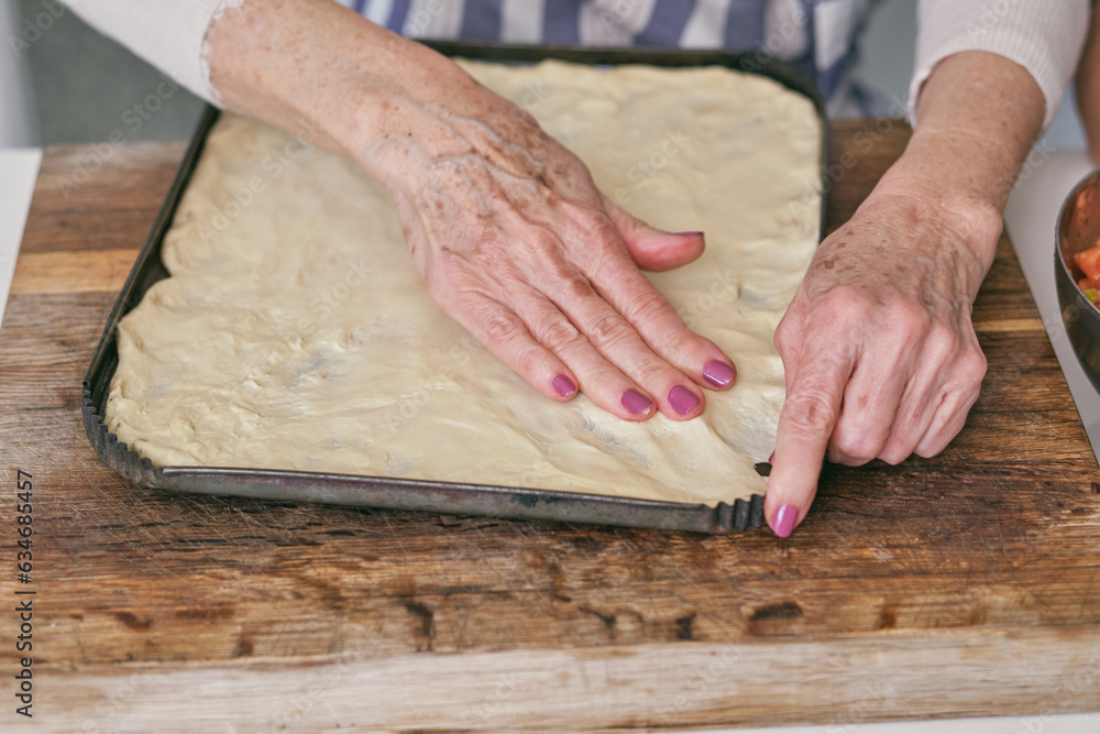 Faceless woman spreading dough on baking pan