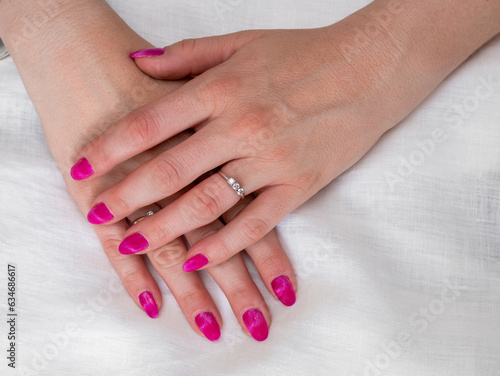 Close-up of well-groomed female pink nails. Beautiful clear fingers of a young girl with nice manicure and Glitter Nail Polish. Girl hands on a white background. Girl is wearing two diamond rings.