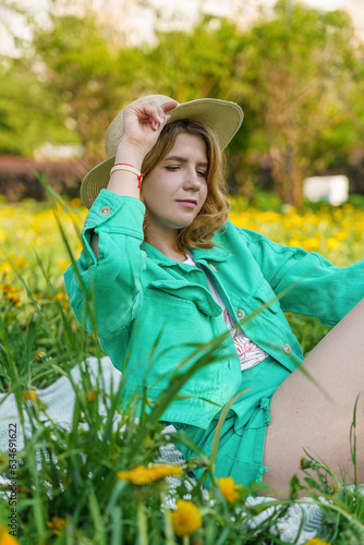 portrait of brunette girl rockin' bright attire and straw hat. She's chillin' in park on picnic blanket, fully enjoying relaxation time. It's all about that weekend vibes, savorin' nature in city photo