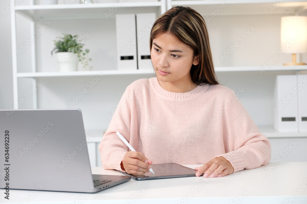 Young asian woman writting on digital tablet while looking at laptop computer, online learning, work from home Young asian woman writting on digital tablet while looking at laptop computer, online learning, work from home