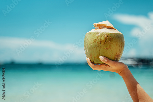 A woman holds a coconut on the background of the sea. Coconut cocktail on the beach. Azure sea