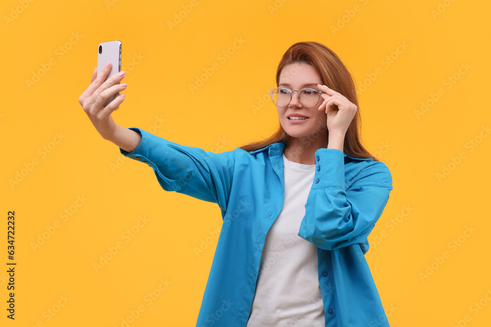 Beautiful woman in eyeglasses taking selfie on orange background Beautiful woman in eyeglasses taking selfie on orange background