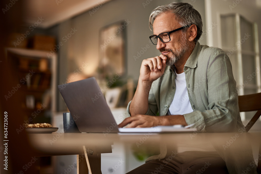 A busy mature man sitting at a wooden desk with a laptop and notebook. A busy mature man sitting at a wooden desk with a laptop and notebook.