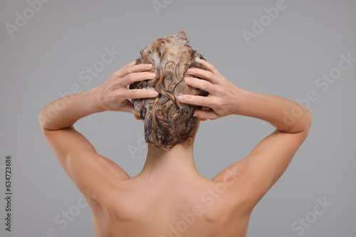 Woman washing hair on light grey background, back view