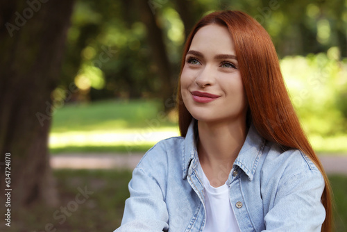 Portrait of beautiful young woman with red hair outdoors. Space for text. Attractive lady posing for camera