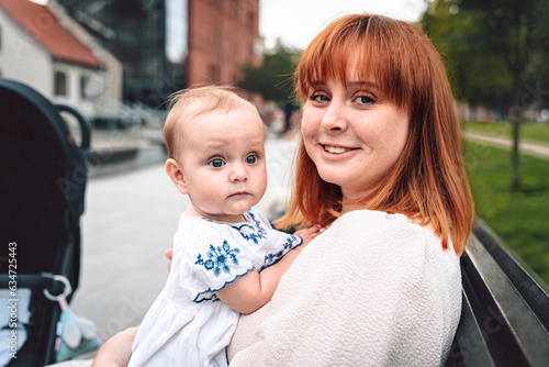 Happy smiling mom with a cute baby on a walk in park. A young woman is holding a child. Everyday life, motherhood