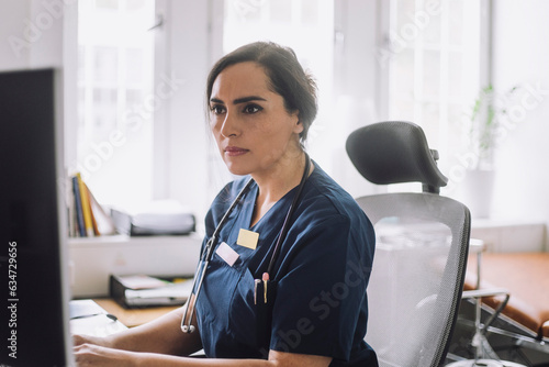 Focused female nurse working while sitting on chair in clinic
