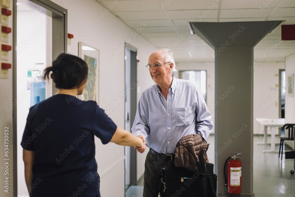 Smiling senior man greeting female medical staff standing at hospital Smiling senior man greeting female medical staff standing at hospital