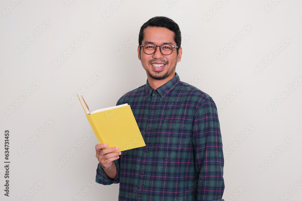 Adult Asian man smiling confident while holding a book Adult Asian man smiling confident while holding a book