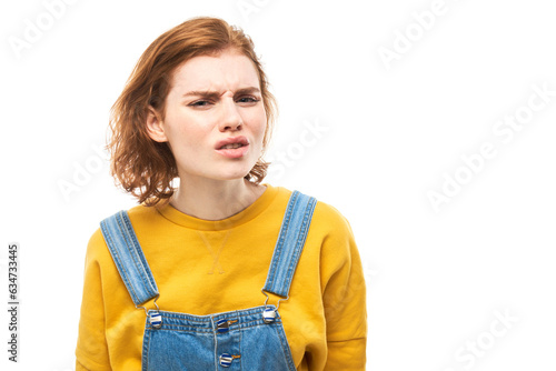 Portrait of young redhead woman in yellow casual suspiciously looking at camera isolated on white studio background, squinting incredulously photo
