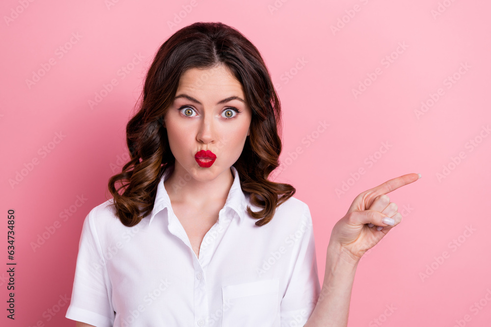 Photo of excited funny young lady wear white shirt pouted lips showing finger empty space isolated pink color background Photo of excited funny young lady wear white shirt pouted lips showing finger empty space isolated pink color background