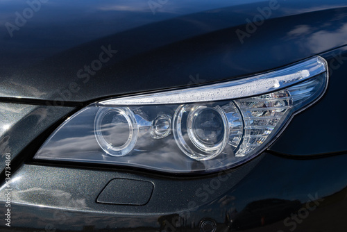 LED Headlight On A Black Car. Black modern car headlight close up on black background.