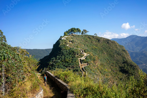 A girl from behind hikes alone through the mountains of Bandipur in Nepal on a trail. It's a sunny day with blue sky photo