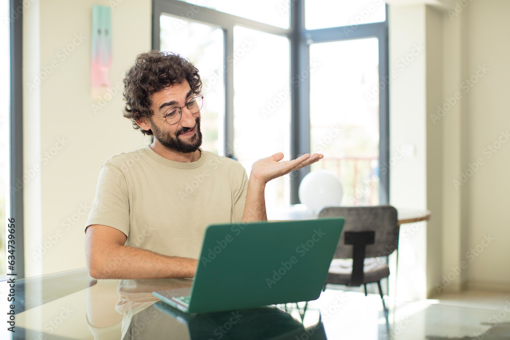 young adult bearded man with a laptop smiling, feeling confident, successful and happy, showing concept or idea on copy space on the side young adult bearded man with a laptop smiling, feeling confident, successful and happy, showing concept or idea on copy space on the side