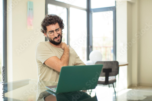 young adult bearded man with a laptop feeling tired, stressed, anxious, frustrated and depressed, suffering with back or neck pain