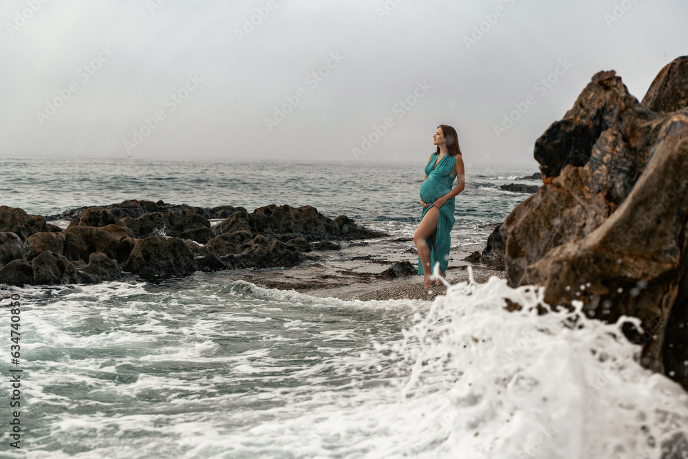 Pregnant woman posing in the long dress at Andalusian coast next to the sea
