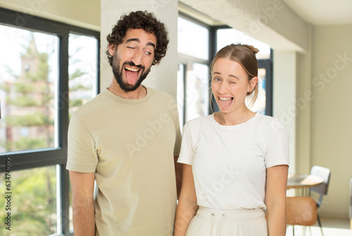 young adult couple with cheerful, carefree, rebellious attitude, joking and sticking tongue out, having fun