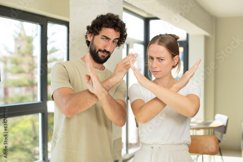 young adult couple looking annoyed and sick of your attitude, saying enough! hands crossed up front, telling you to stop