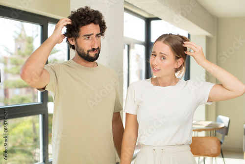 young adult couple feeling puzzled and confused  scratching head and looking to the side
