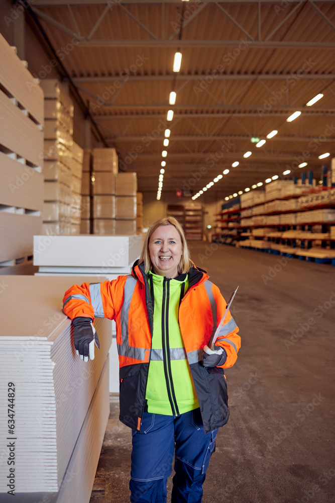 Portrait of happy blue-collar worker in protective workwear leaning on planks in distribution warehouse Portrait of happy blue-collar worker in protective workwear leaning on planks in distribution warehouse