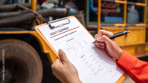 Action of a mechnical engineer is using a pen to mark at need repair on the heavy machine inspection form. Industrial service working concept. Selective focus. 