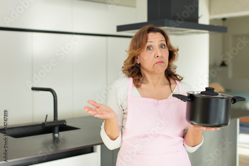middle age pretty woman shrugging, feeling confused and uncertain. cooking at home concept
