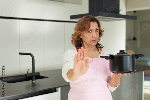 middle age pretty woman looking serious showing open palm making stop gesture. cooking at home concept