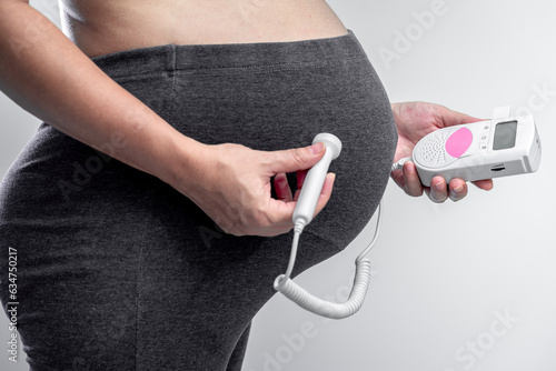 Close-up of pregnant woman using pocket fetal doppler to monitor baby heart beat at home, For baby healthcare with fetal doppler concept.